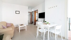 Un salon comprenant un canapé, une table à manger avec des chaises, un téléviseur fixé au mur et une porte donnant sur une autre pièce.