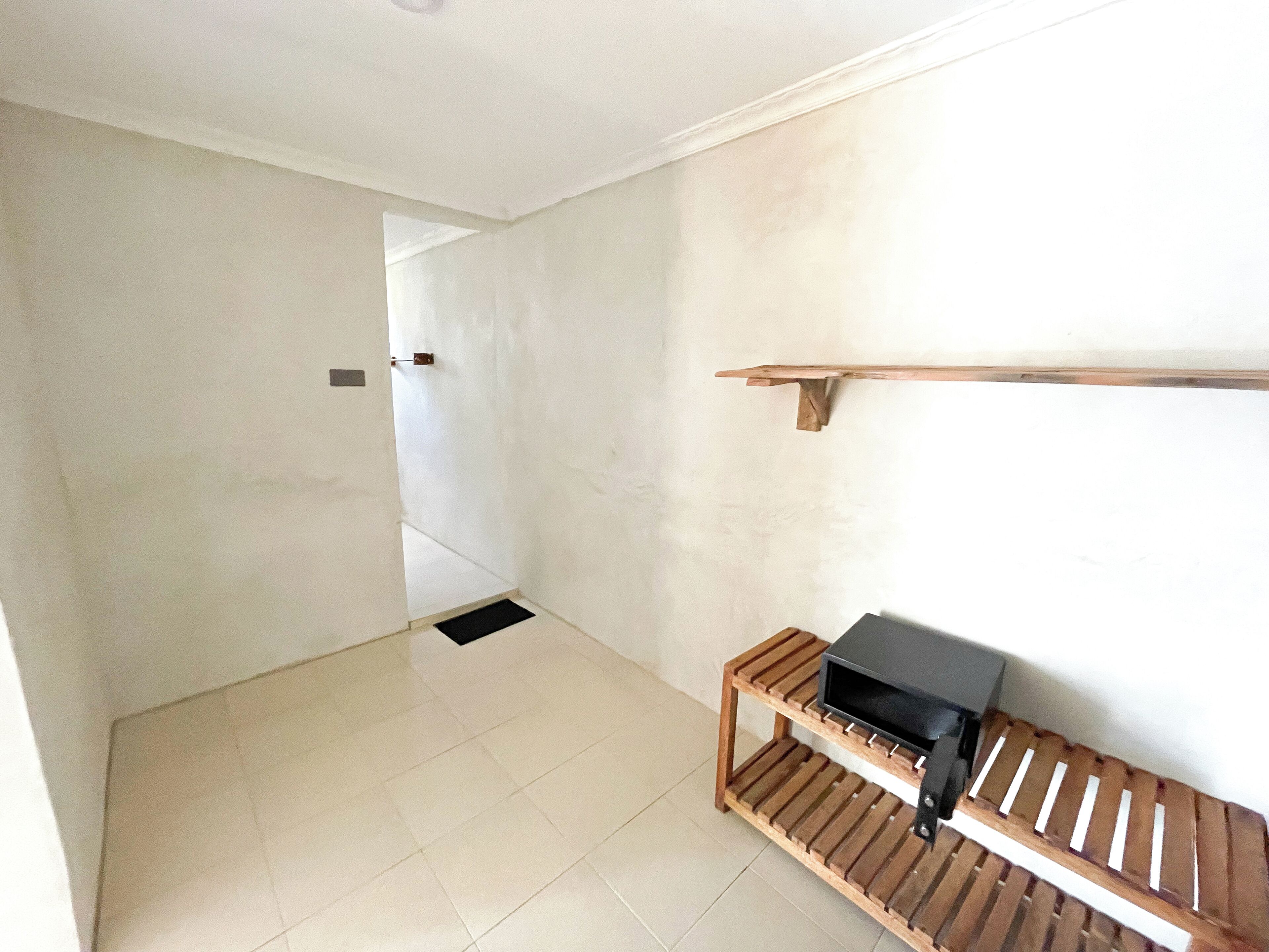 Un couloir avec un banc en bois, un objet noir posé sur le banc et une étagère en bois fixée au mur.