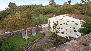 Un muro di pietra, un edificio bianco con motivi in pelle di vacca, una sedia e un piccolo albero.