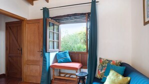 Una stanza con una panca in legno, uno sgabello, un divano blu e una finestra con tende.