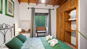 Camera da letto con un letto, cuscini verdi, una panca, un armadio in legno e una finestra vista verde.