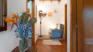 Un corridoio con soffitto in legno, un tappeto decorato, un vaso con fiori, una libreria e una poltrona con motivo decorativo.