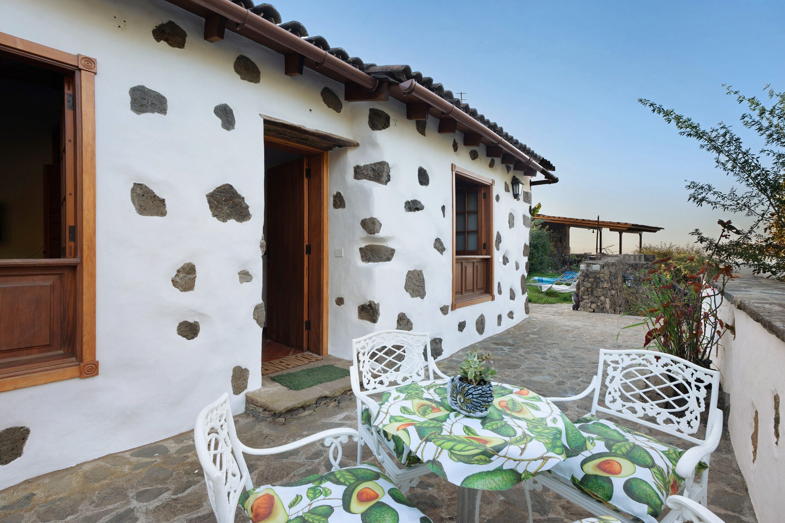 Una casa in pietra con facciata bianca, porte in legno e un patio con sedie e tavolo in metallo bianco.