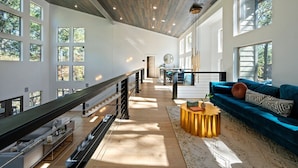 A spacious interior with a wooden ceiling, large windows, a blue sofa, and a staircase.