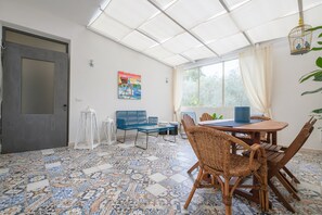 A room with a tiled floor, a dining table with chairs, a bench, a door, and a window with curtains.