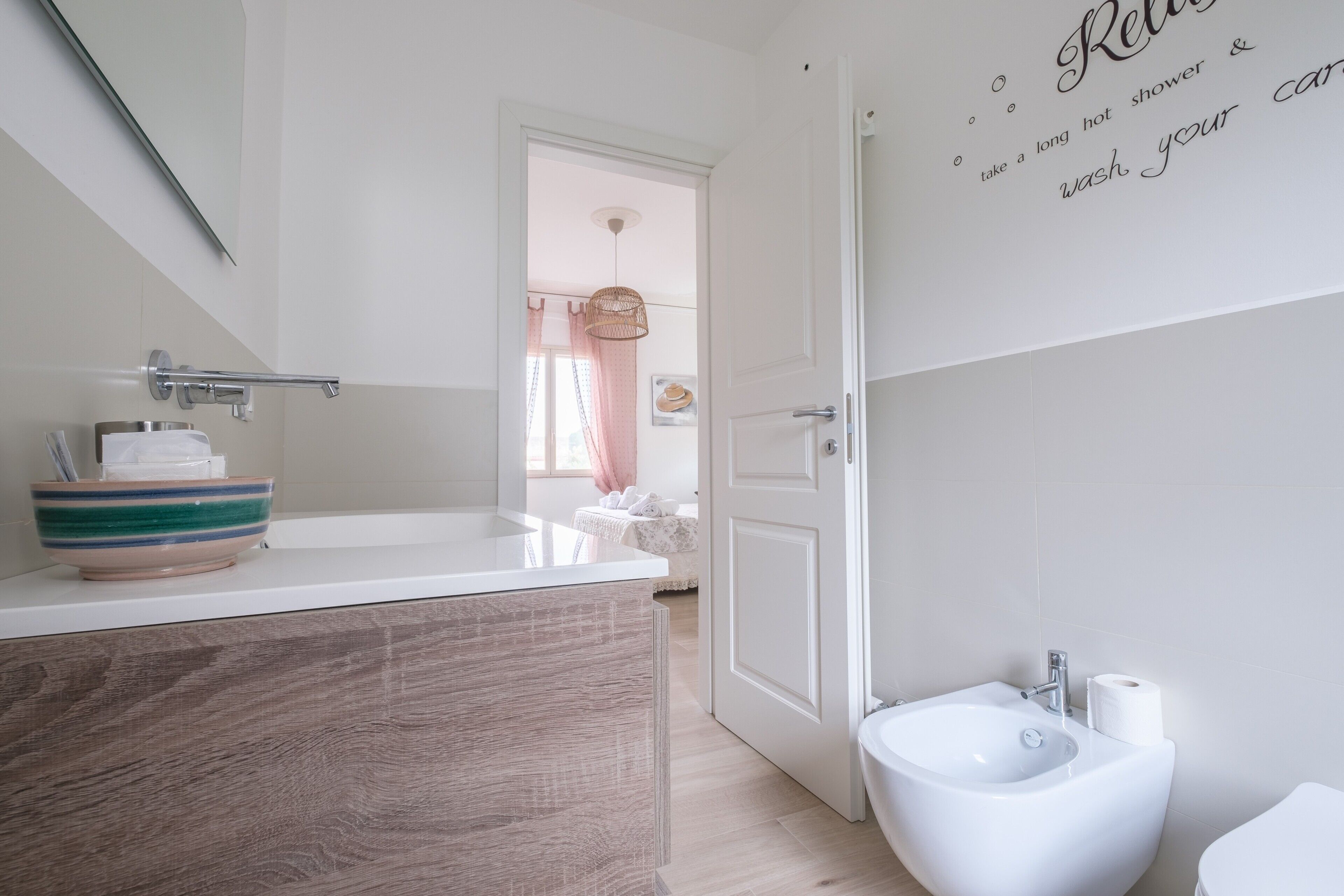 A bathroom with a white sink, a bidet, and a toilet. There is a mirror above the sink, and a door leading to another room.