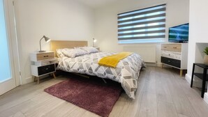 Et moderne soveværelse med seng, natborde, et fjernsyn og et vindue med skodder.