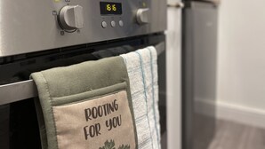 En ovn med et digitalt ur der viser 16:16, en træbordplade over, og et håndklæde med teksten "ROOTING FOR YOU" hængende på ovnens dør.
