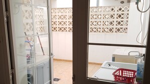 Una cocina con un lavamanos de acero inoxidable, una ventana con vistas a un área de lavandería y una puerta que da a un balcón.