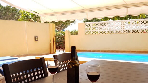 Un área de estar al aire libre con una mesa, sillas y una botella de vino.