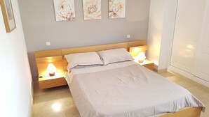 Una cama bien hecha con un cabecero de madera, dos lámparas de noche y tres cuadros florales colgados en la pared.