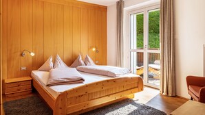A bedroom with a wooden bed, a nightstand, a desk, and a view through a glass door to an outdoor area. - Holiday Apartment "Salman" with Mountain View, Balcony & Wi-Fi (Ortisei)