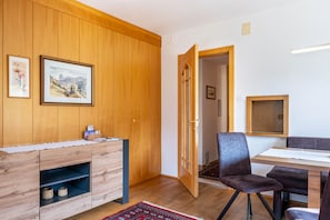 A room with wooden paneling, a dining table with chairs, a cabinet with shelves, and a door leading to another room.