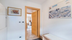 Un couloir avec une porte en bois, un tableau encadré, un banc et une affiche accrochée au mur.