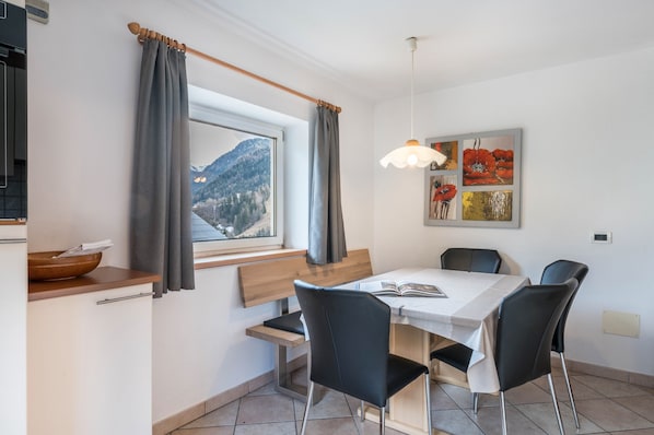 A dining area with a table, chairs, a bench, a window with curtains, and a painting on the wall.