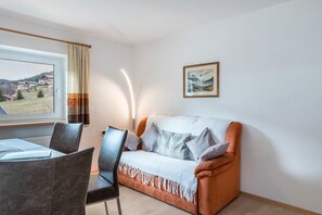 A room with a sofa, a dining table with chairs, a window with curtains, and a framed picture on the wall.