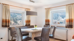 Un espace repas comprenant une table, des chaises et offrant une vue sur un paysage montagneux grâce à de grandes fenêtres.