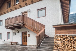 A building with a wooden staircase, a door with a number, and a stack of firewood.