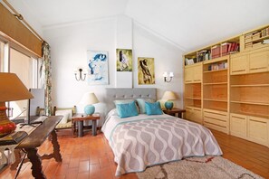 A bedroom with a bed, bedside tables, lamps, a wooden bookshelf, and artwork on the walls.