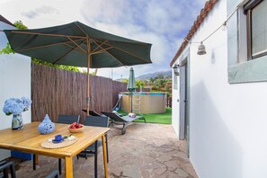 Une terrasse avec une table, des chaises, un grand parasol, un jacuzzi et une clôture en bois.
