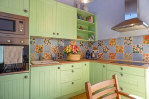Une cuisine avec des armoires vertes, un four à micro-ondes, une cuisinière et une chaise en bois.