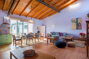 Un vaste espace de vie doté d’un plafond en bois, d’une table à manger avec des chaises, d’un canapé et d’un coin cuisine avec un meuble vert.