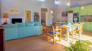 En rummelig opholdsstue med sofa, spisebord, stole og et køkken med skabe og hårde hvidevarer.