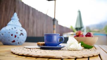 A table with a blue cup, a white flower, and a bowl of fruit.