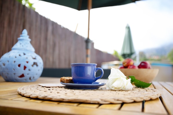 Een tafel met een blauw kopje, een witte bloem en een schaal met fruit.