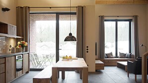 A modern kitchen with a dining area, large windows, and a view of the outdoors.