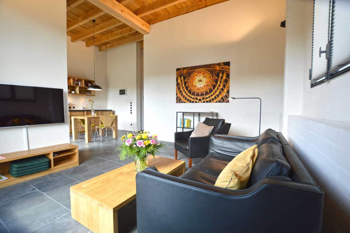 Un salon moderne avec un canapé en cuir noir, une table basse en bois, un téléviseur et un tableau accroché au mur.