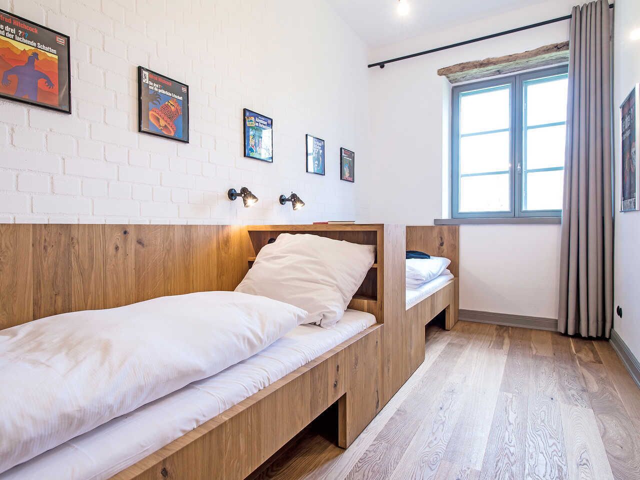 A bedroom with a wooden bunk bed, a small desk, and a window with curtains.