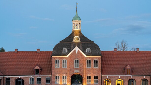 A large brick building with a prominent clock tower and a central archway.