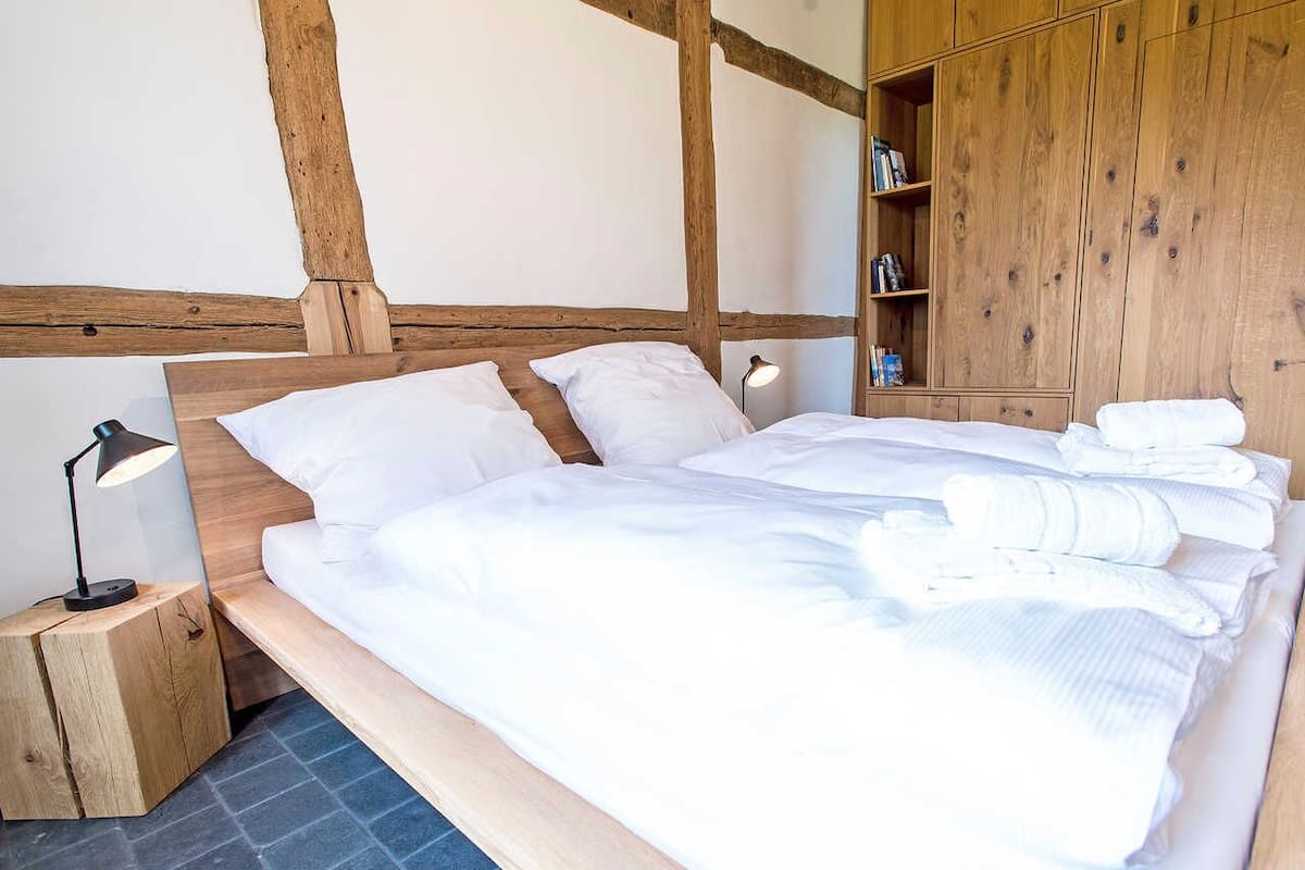 Un lit avec du linge de lit blanc, une tête de lit en bois et une table de chevet avec une lampe.