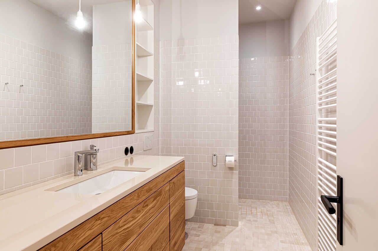 A modern bathroom with a white tiled shower, a wooden vanity, and a large mirror.