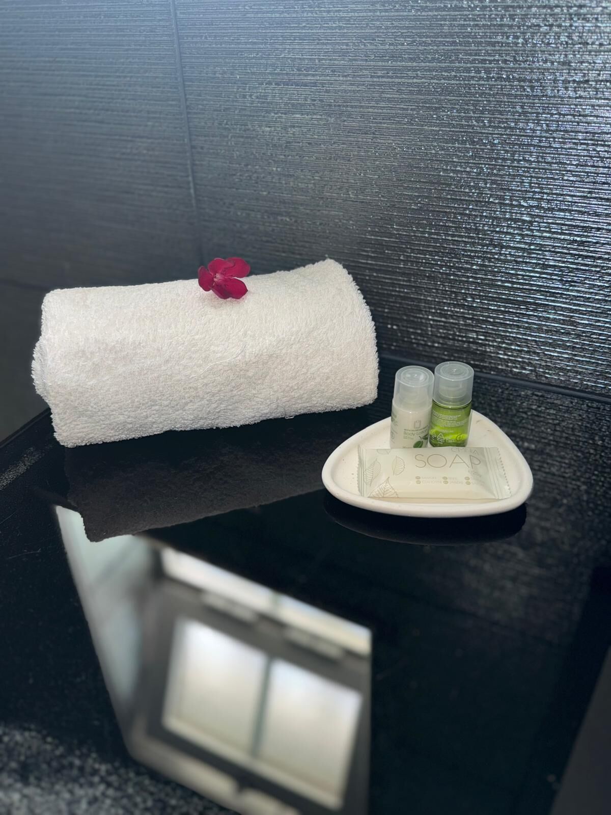 A white towel with a red flower on a black countertop, next to a soap dish with two bottles.