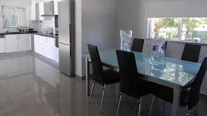 A modern kitchen with white cabinets, a stainless steel refrigerator, and a glass dining table with black chairs. - PRIVATE VILLA WITH POOL IN THE ALGARVE AT OLHAO NEAR FARO (OLHAO)
