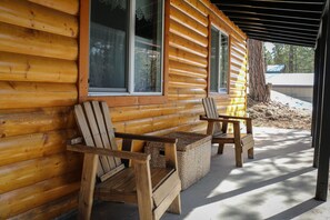 Eine Blockhütte mit zwei Holz-Adirondack-Stühlen davor, einer Laube und Blick auf eine verschneite Landschaft.