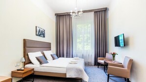 A hotel room with a bed, a desk, a chair, a TV, and a window with curtains. - Aparthotel Old Town (Kraków)