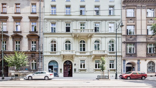 A multi-story building with a classical architectural style, featuring a central entrance with a dark door, arched windows, and a balcony with ornate railings. - Aparthotel Old Town (Kraków)