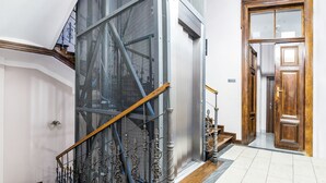 A staircase with a wooden handrail, a metal mesh barrier, and a wooden door at the bottom. - Aparthotel Old Town (Kraków)