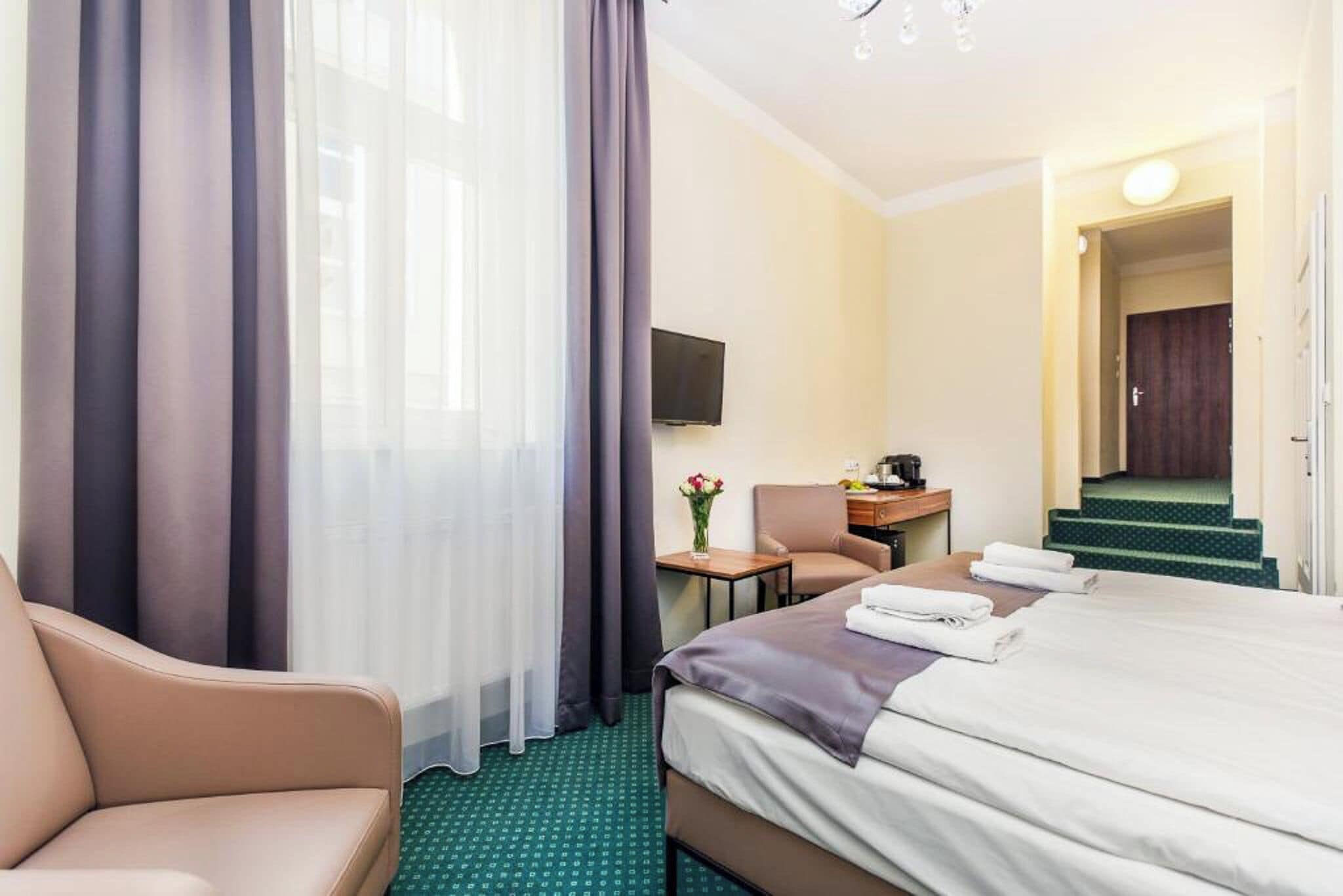 Una habitación de hotel con cama, una silla, un escritorio con computadora, televisor y una escalera.