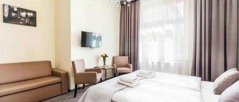 A hotel room with a bed, a sofa, two armchairs, a TV, and a chandelier.