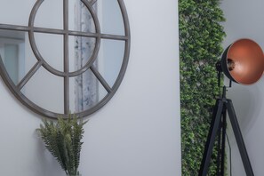 A room with a round mirror, a tripod lamp, and a wall-mounted plant.
