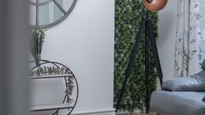 Una habitación con un sofá gris, un espejo redondo, una lámpara de pie y una pared con follaje verde.