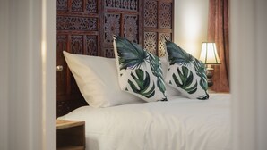 Una cama con ropa blanca y dos almohadas decorativas con motivos de hojas tropicales.