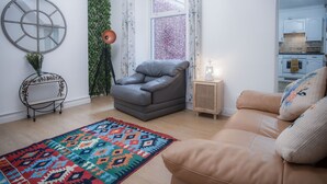 Un salón con un sofá, un sillón gris, un tapete colorido, un espejo redondo y una planta en la pared.