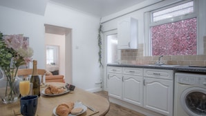 Una cocina moderna con armarios blancos, lavadora integrada y comedor con mesa dispuesta para el desayuno.