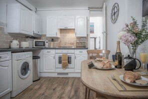 A kitchen with white cabinets, a microwave, a toaster, a sink, and a dining table with breakfast items.