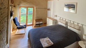 Ein Schlafzimmer mit einem großen Bett, Holzboden, Steinwand und Blick auf Grünflächen.